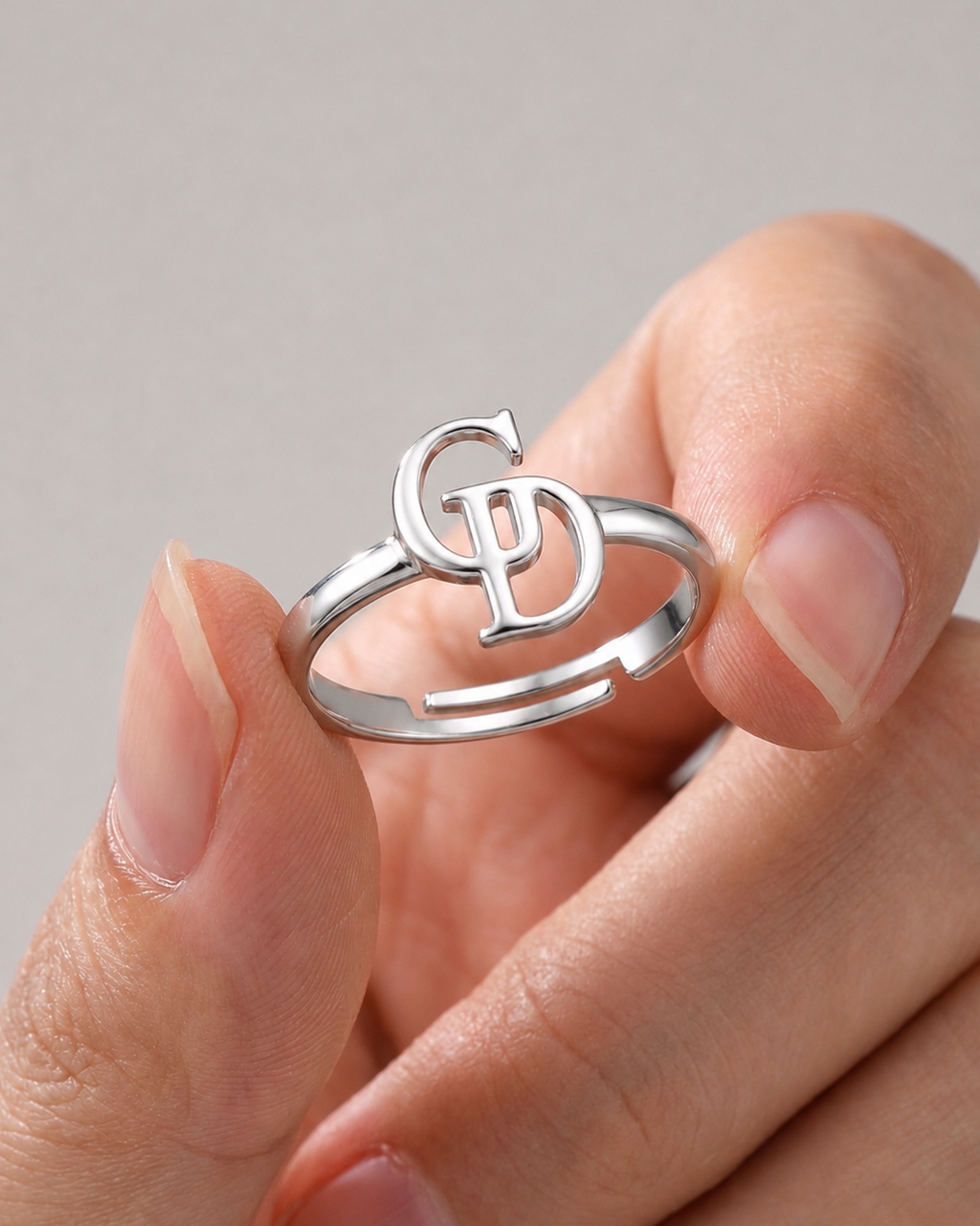 A close-up of a hand holding a silver open-ring band with a stylized interlocking 'G' and 'P' monogram design on top.