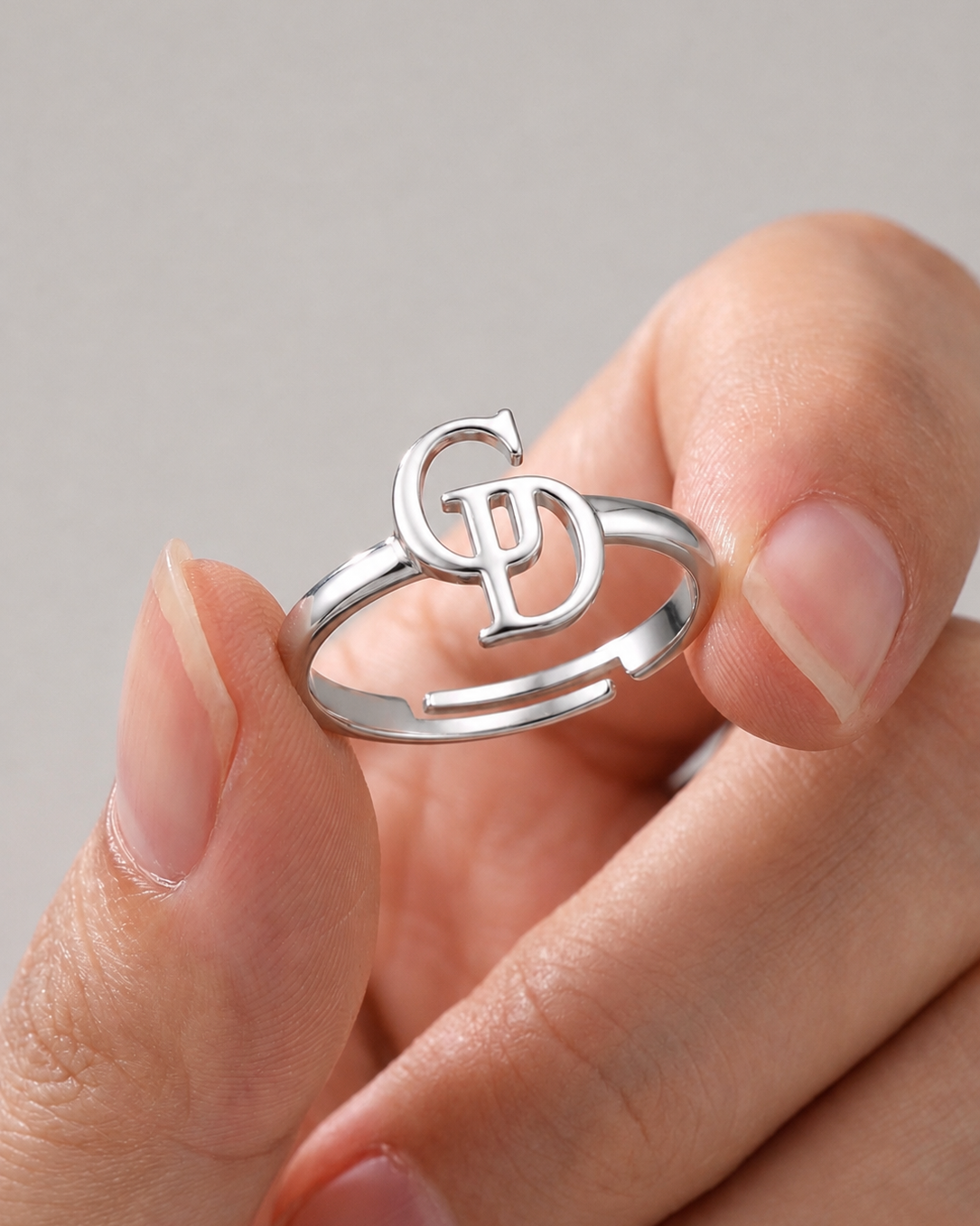 A close-up of a hand holding a silver open-ring band with a stylized interlocking 'G' and 'P' monogram design on top.