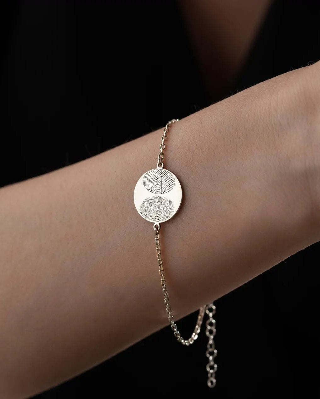 A delicate silver chain bracelet with a circular disc charm featuring a textured yin-yang symbol, shown worn on a person's wrist against a dark background.